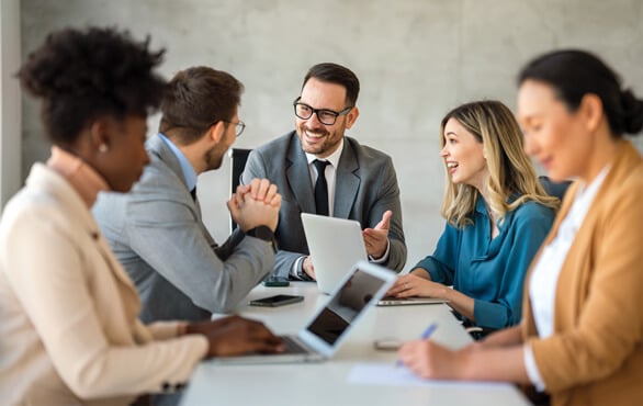 Diverse team of business professionals collaborating in a meeting with laptops, discussing leadership and artificial intelligence strategies for workplace success.