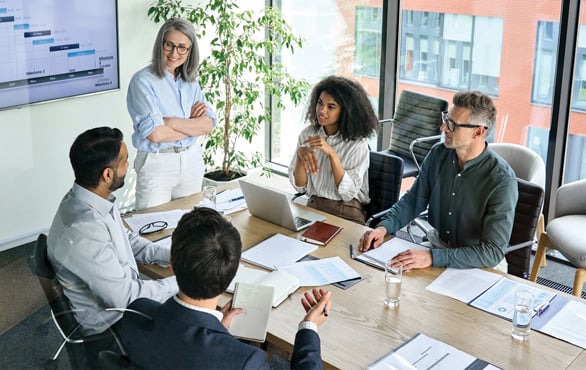Group of business professionals in a conference room meeting, collaborating on leadership and artificial intelligence strategies using laptops and presentation charts.