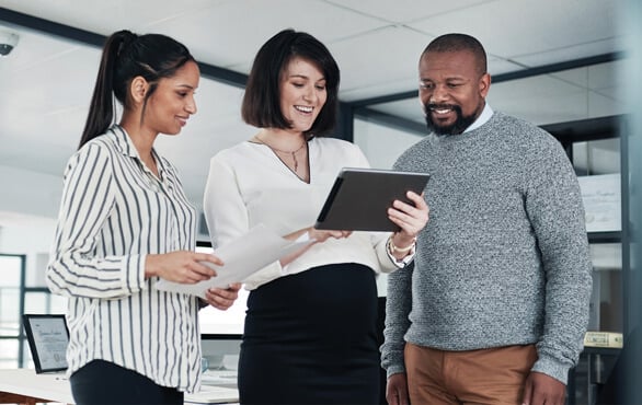 Team of business professionals reviewing documents and discussing strategies on a digital tablet in a modern office.