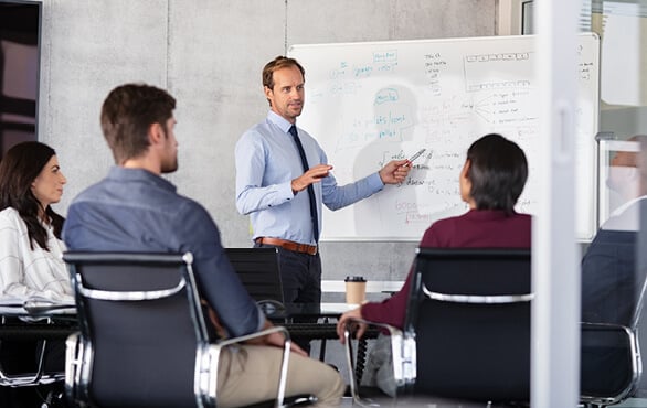 Manager presenting strategic plan on whiteboard to executive team during business strategy session.