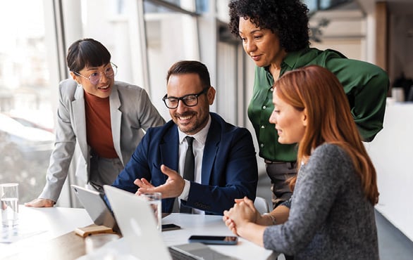 Diverse team of business professionals collaborating around a conference table while reviewing plans and discussing strategy.