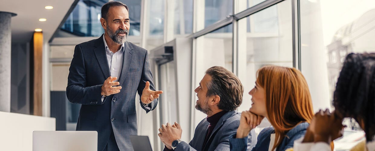 Manager speaking with colleagues during a workplace meeting about employee development and team performance.
