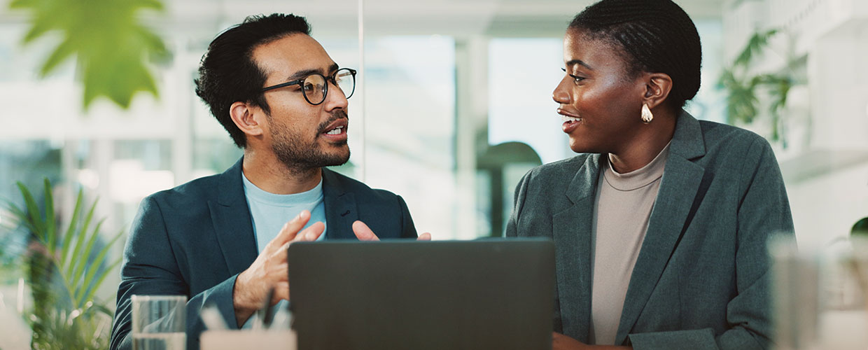 Two professionals discussing ideas in front of a laptop in a modern office, highlighting collaboration, manager coaching and leadership development.