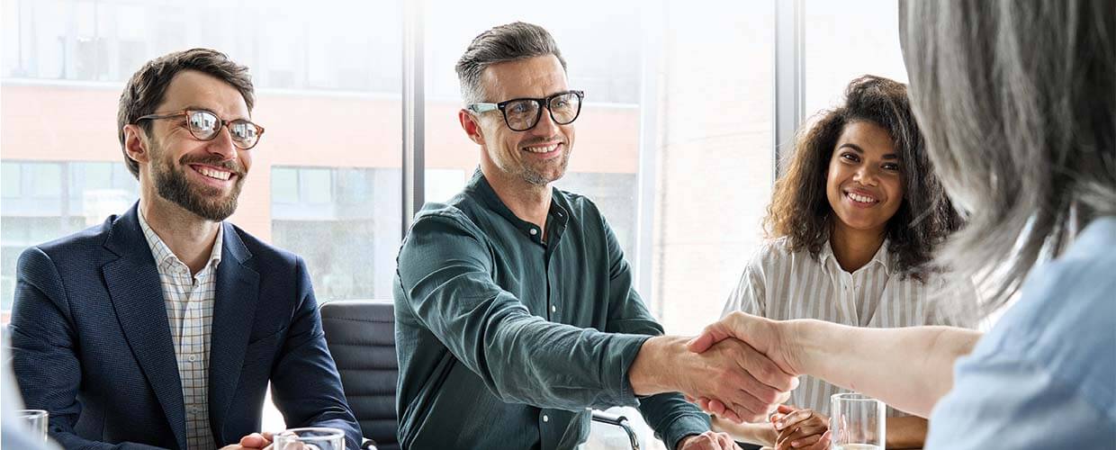 Business professionals smiling during a meeting as two colleagues shake hands, representing workplace trust, collaboration and partnership.