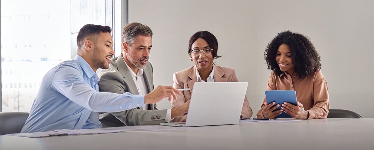 Professional team meeting in a modern office with managers collaborating around a laptop and tablet, discussing employee engagement, leadership strategies, and workplace communication.