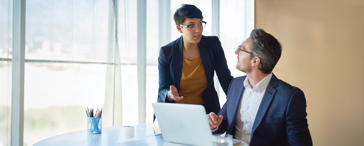 Professional colleagues discussing AI strategy and workplace technology at a laptop in a modern office, highlighting collaboration, leadership decision-making and digital transformation