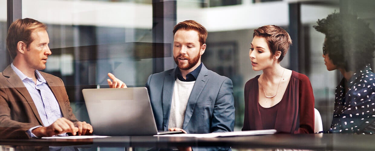 Business professionals collaborating in a modern office, discussing strategy and reviewing data on a laptop during a team meeting