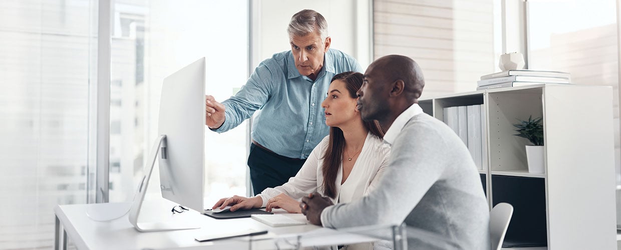 Three colleagues reviewing information on a computer during a workplace learning session.