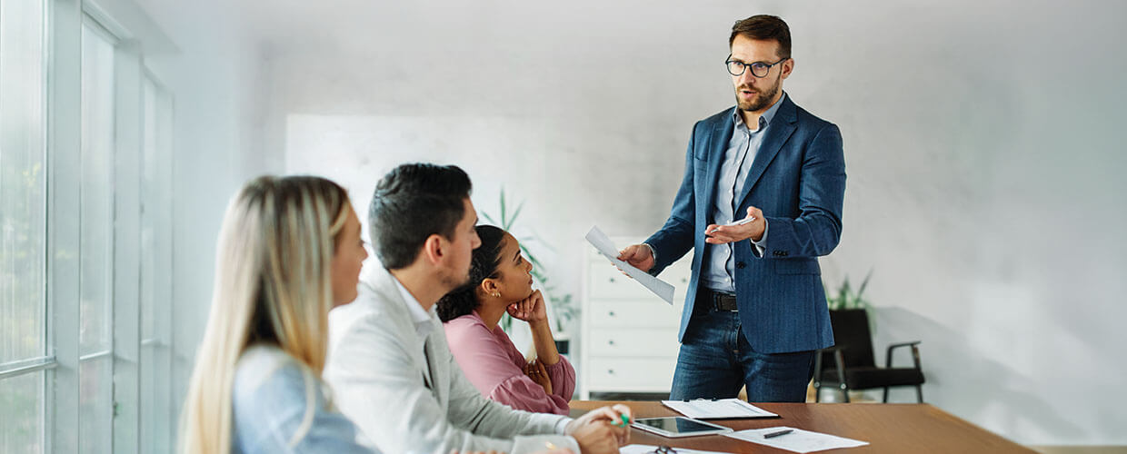 Manager leading a workplace discussion with three employees, illustrating leadership communication, employee coaching and professional development.