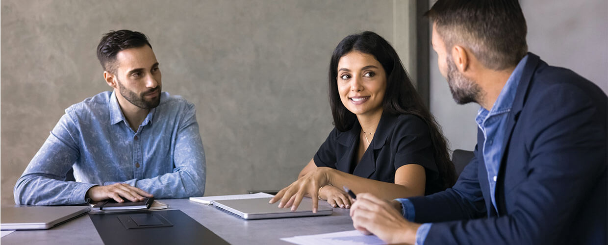 Three professionals collaborating during a workplace meeting, discussing ideas and strategies for talent development and AI skills.