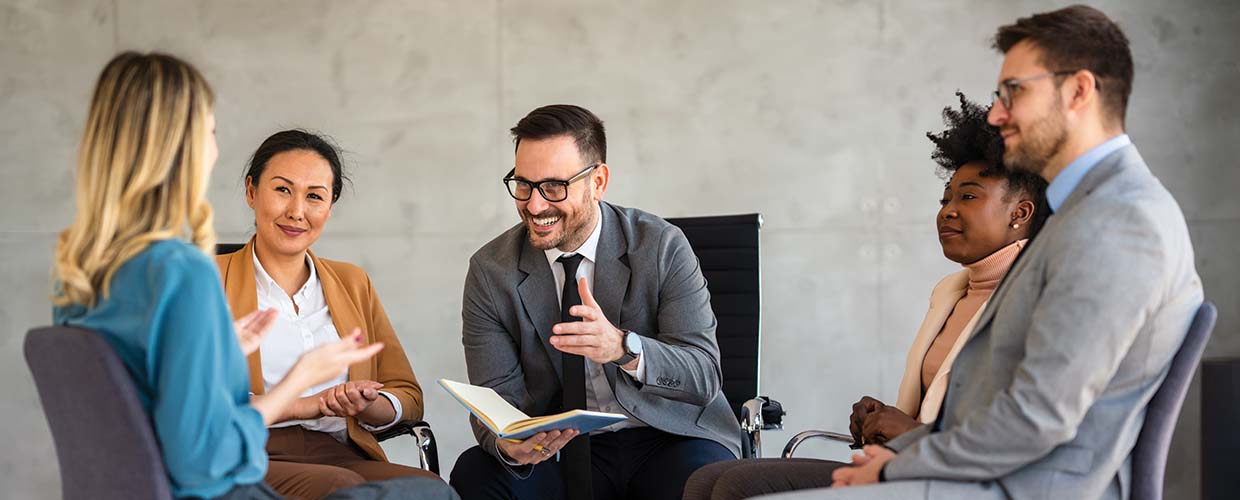 Diverse group of five business professionals engaged in a workplace discussion, demonstrating collaboration, communication and leadership development.