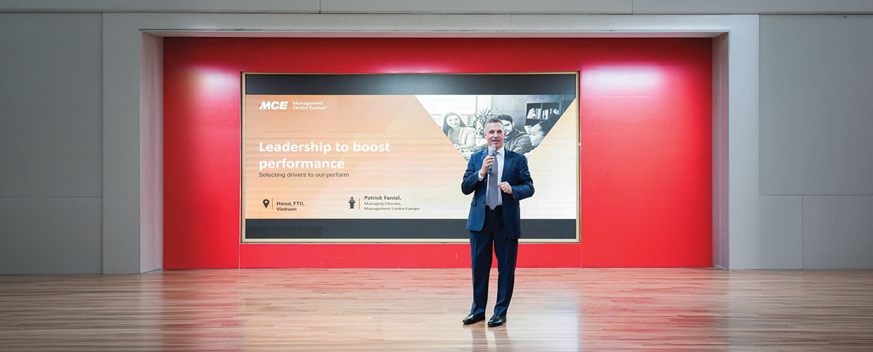 Business leader presenting leadership strategies on stage at a Management Centre Europe event focused on improving organizational performance.