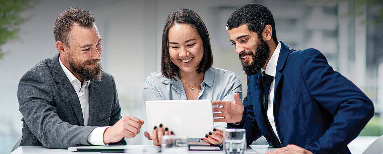 Business professionals collaborating over a tablet in a modern office meeting setting.