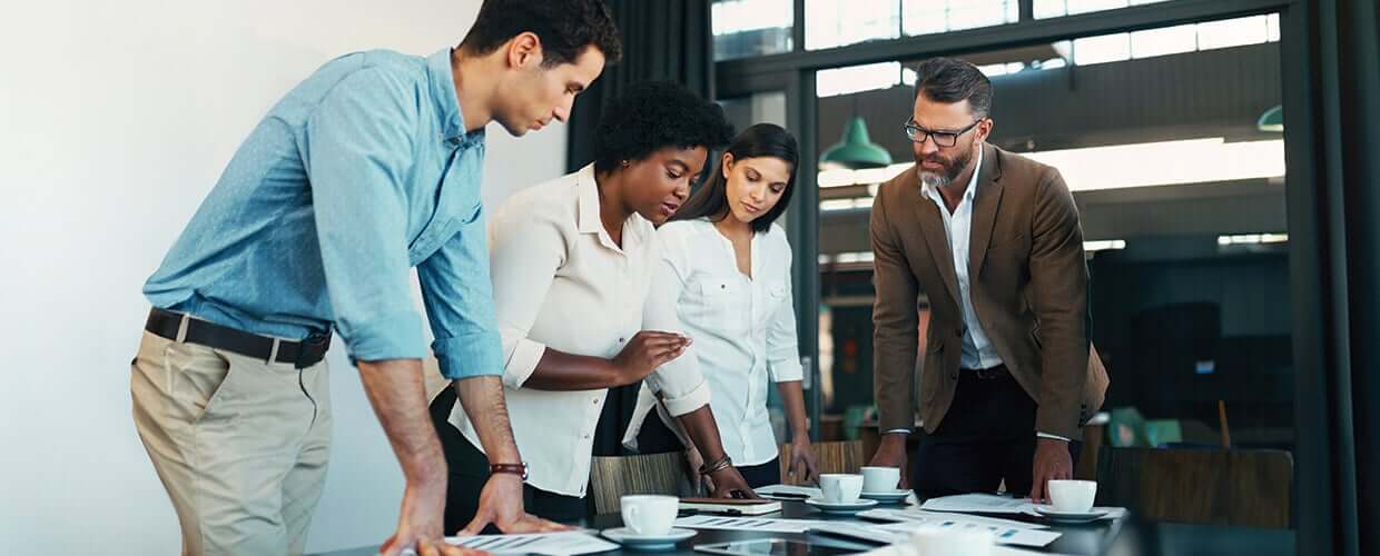 Team of professionals collaborating on a business project, reviewing documents together in a modern office setting.