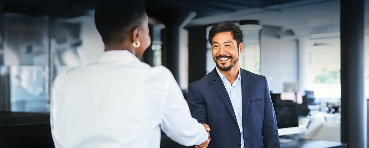 Smiling business professionals greeting each other with a handshake in a modern office environment.