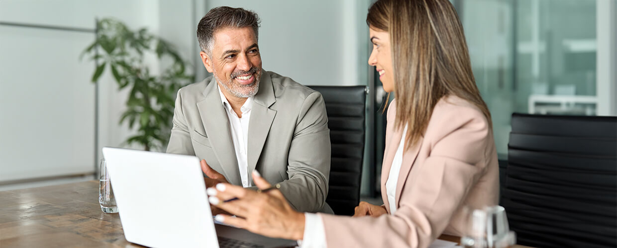 Smiling business professionals having a discussion at a conference table with a laptop in a modern office.