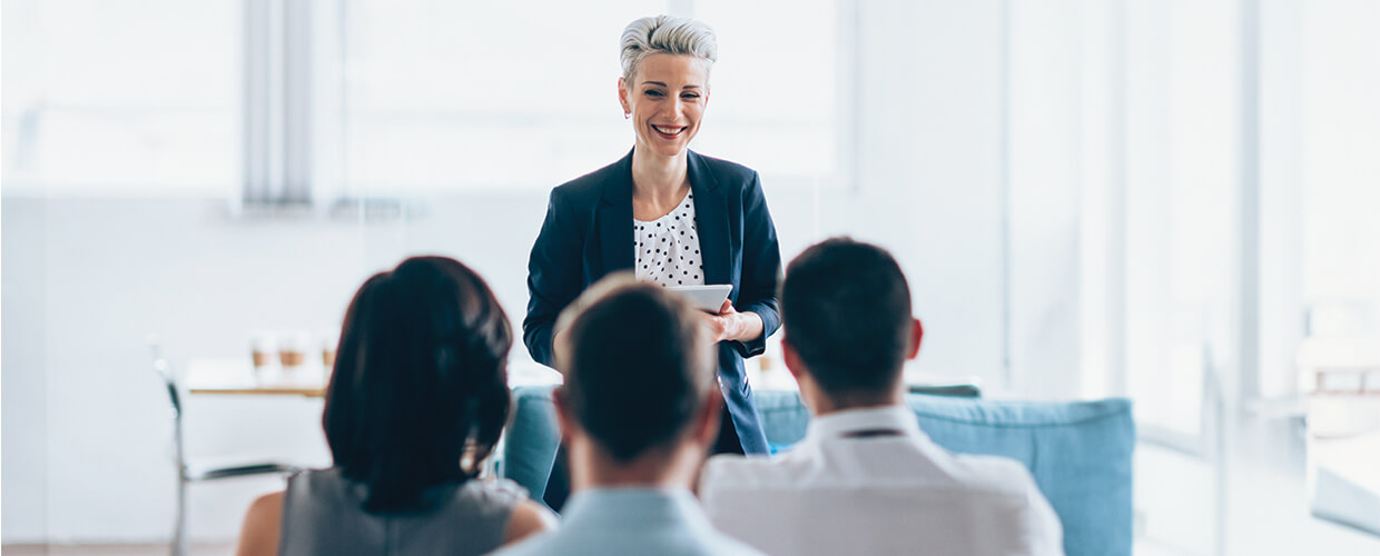 Businesswoman leading a professional training session, speaking to a group of employees in a bright modern office.