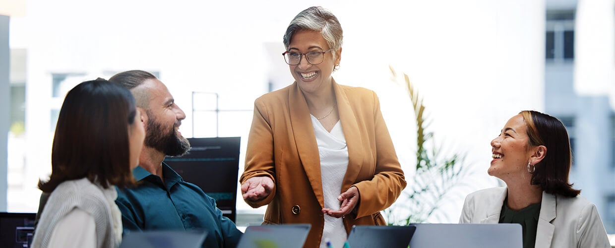 Senior leader facilitating a collaborative meeting with a multigenerational team in a modern workplace, highlighting inclusive leadership and cross-generational communication.