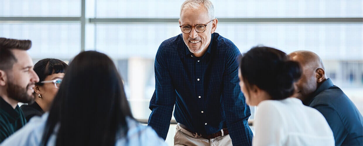 Experienced leader facilitating a team discussion in a modern workplace, demonstrating collaborative leadership and cross-generational teamwork.