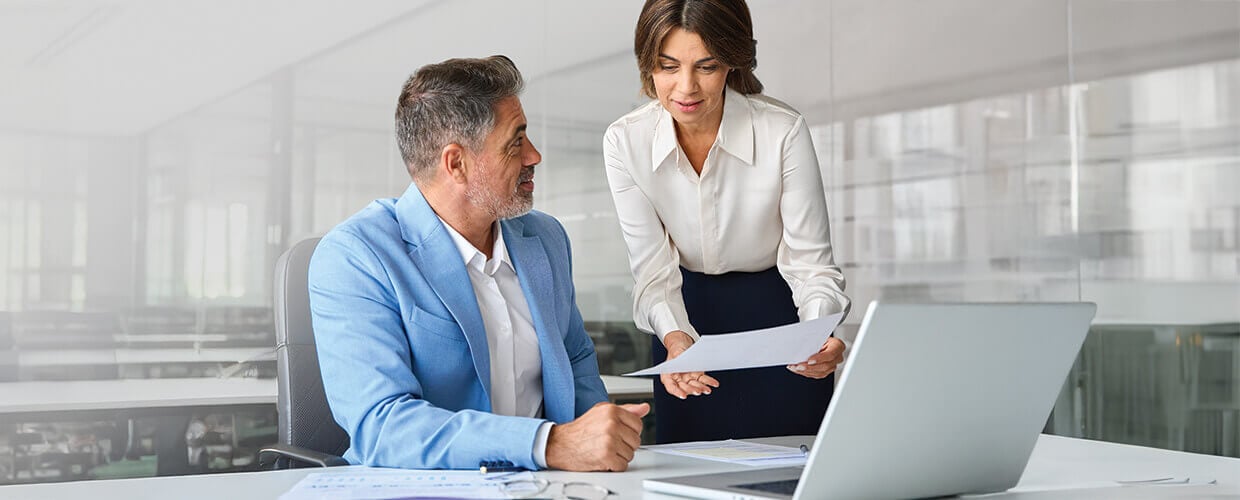 Manager reviewing documents with a colleague in a modern office, showcasing professional collaboration, leadership communication, and workplace learning.